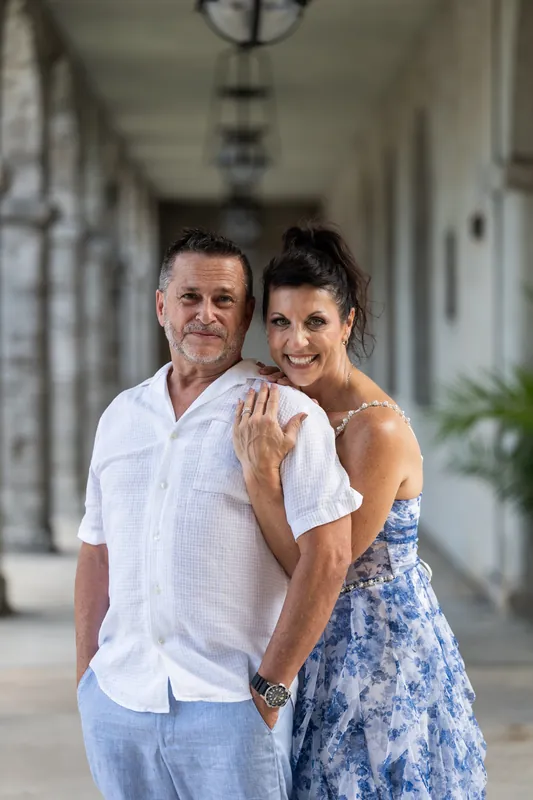 Brian stands behind Mary with his arm around her shoulder, both smiling at the camera under the museum's covered archway.