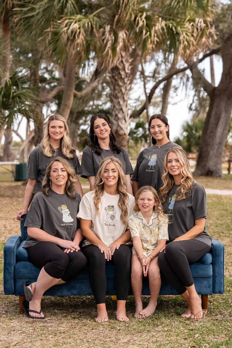 Bridal party sitting on blue couch outdoors with palm trees behind them