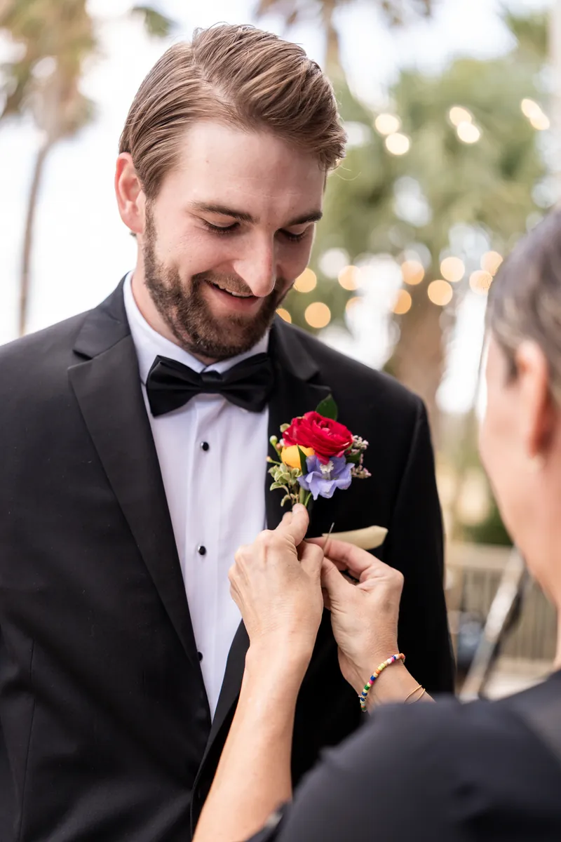 Groom getting colorful boutonniere pinned to his lapel