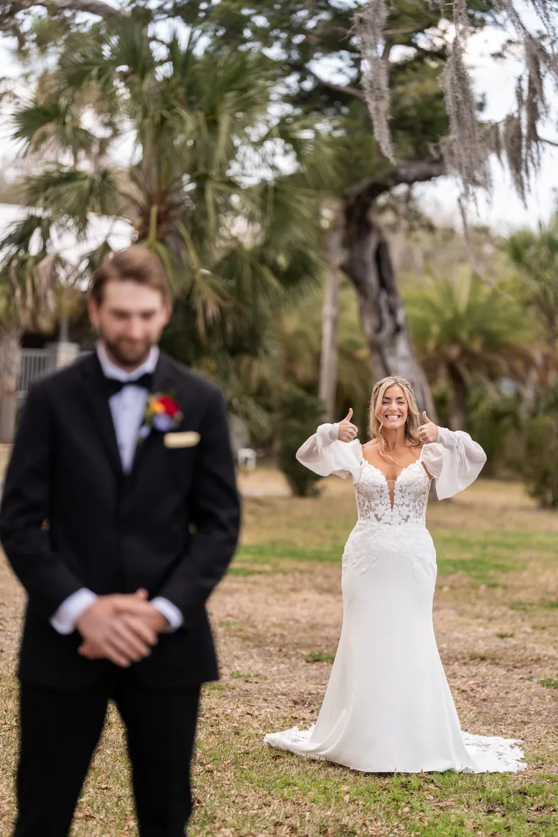 Bride giving two thumbs up behind groom before first look reveal