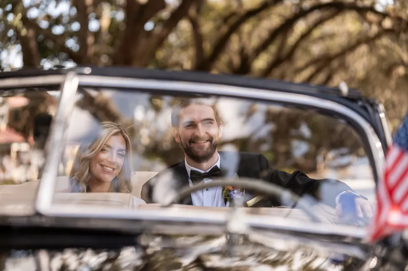 Couple sitting in vintage black convertible under oak canopy