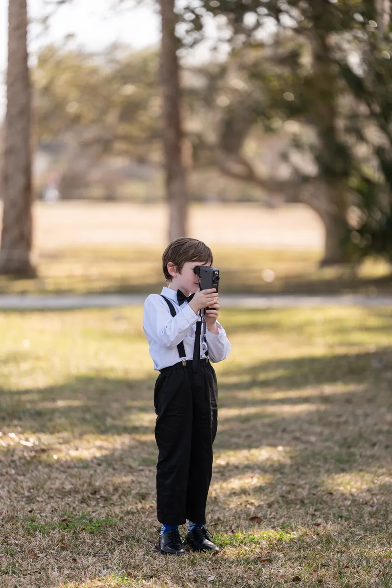 Ring bearer in suspenders filming with camera