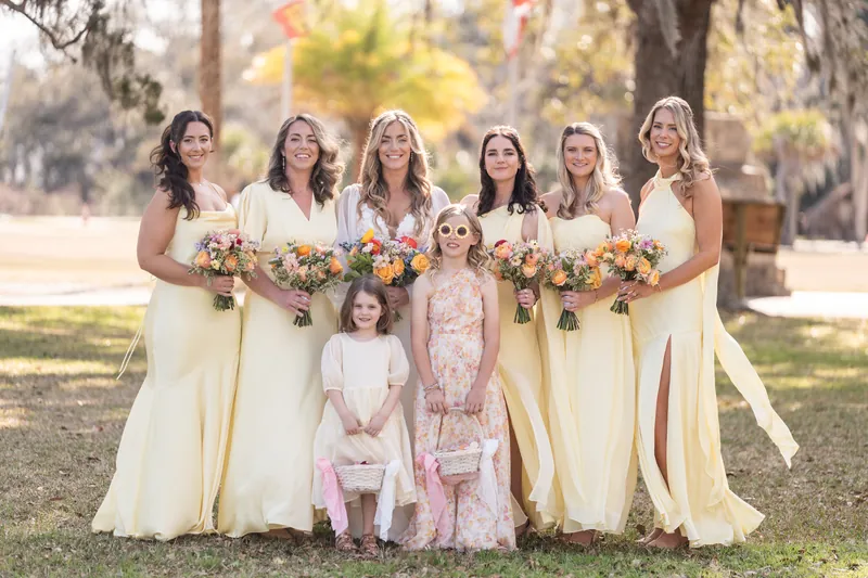Bridal party with bride in yellow dresses holding colorful bouquets with flower girls