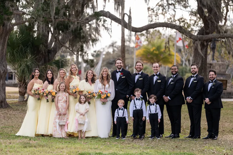 Full wedding party under oak trees with yellow bridesmaids and ring bearers in suspenders