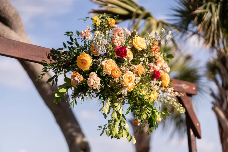 Ceremony arbor floral arrangement with yellow and red roses and trailing greenery