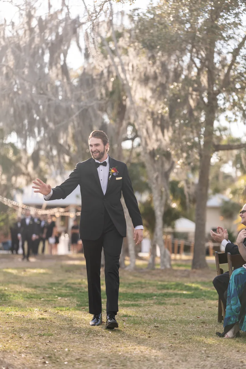 Groom walking down aisle greeting guests with open arms and a smile