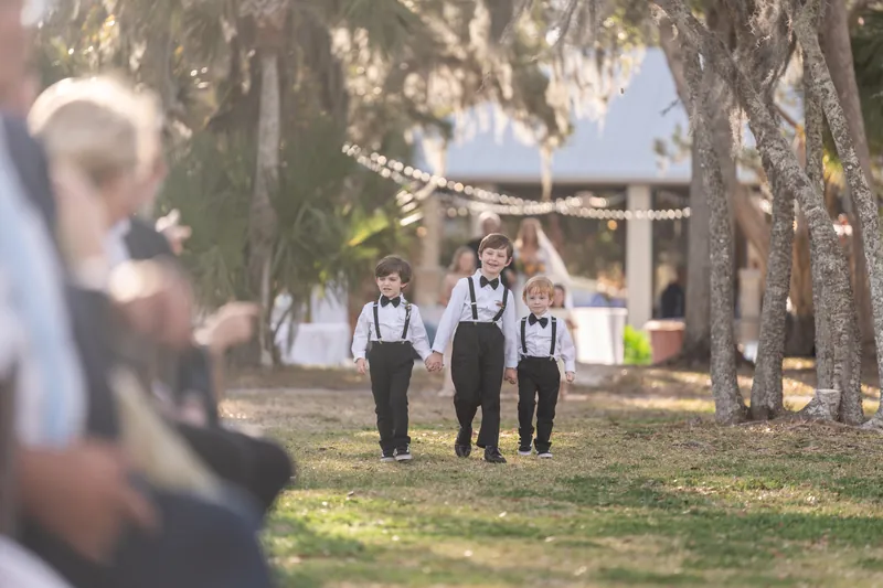 Three ring bearers in suspenders and bow ties walking down the aisle hand in hand