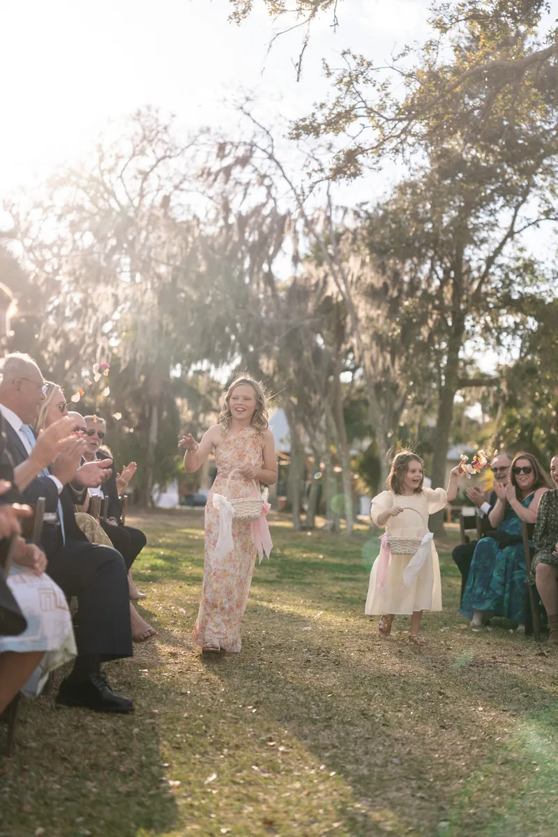 Two flower girls tossing petals as backlit sun streams through Spanish moss