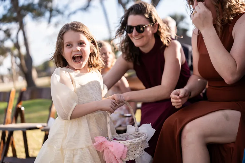 Flower girl laughing with basket beside seated guests