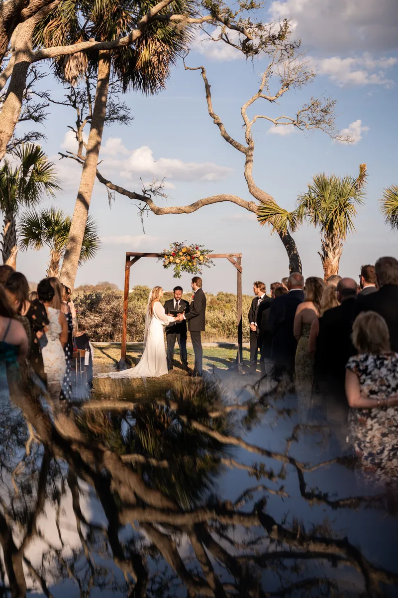 Ceremony reflected in water puddle with palms and sky silhouetted