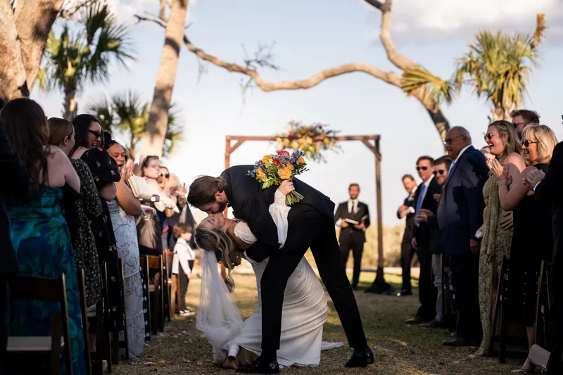 Recessional dip kiss in the aisle with guests cheering and arbor behind them