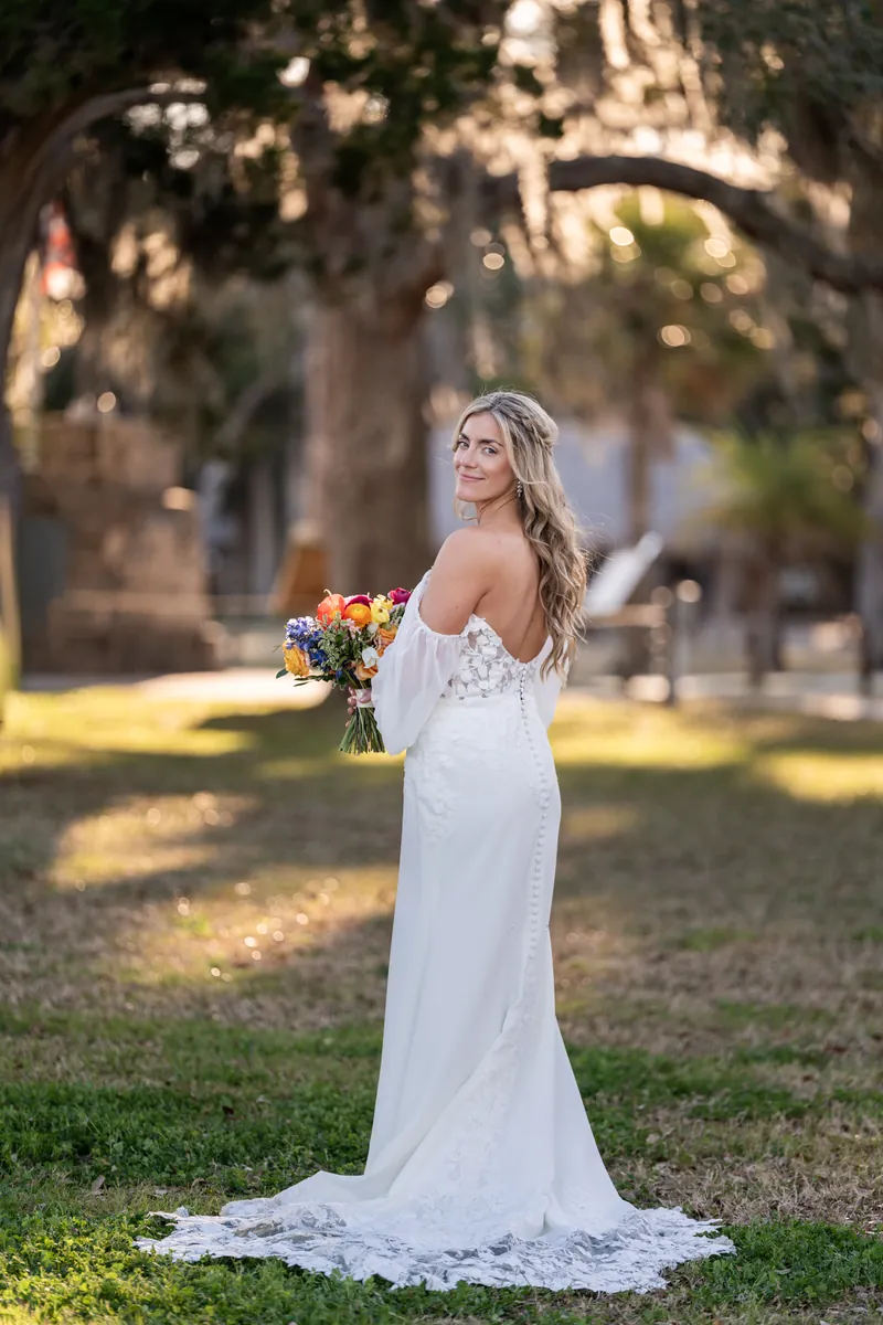 Bride from behind showing dress back details and bishop sleeves with bouquet