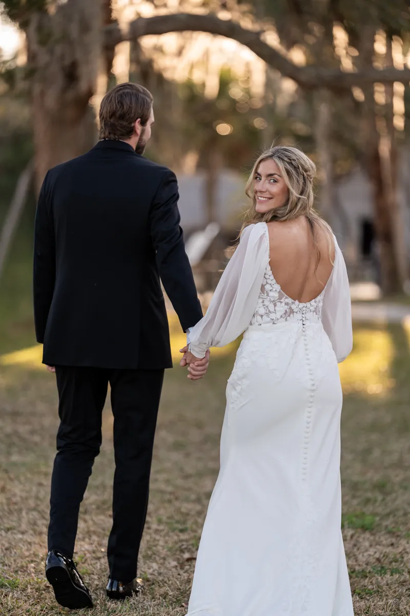 Couple walking hand in hand as bride looks back over her shoulder smiling