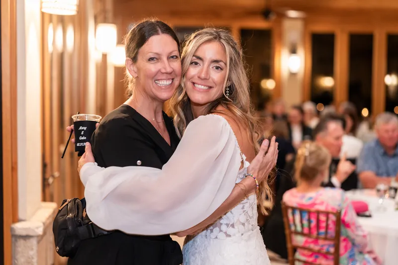 Bride hugging friend holding custom koozie inside reception pavilion
