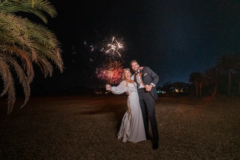 Couple posing with fireworks exploding behind them under palm fronds
