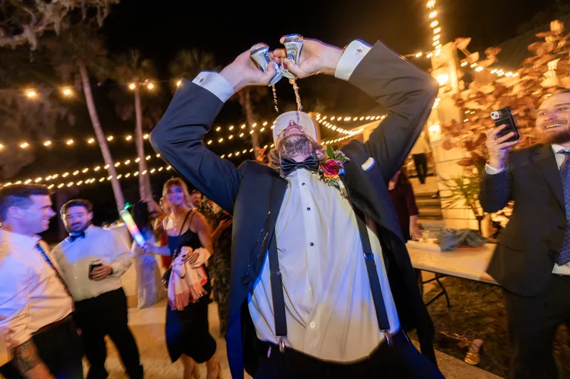 Groom double-fisting beers on dance floor with suspenders down