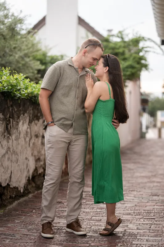 Couple embraces on a shaded brick street lined with white stone walls and foliage.