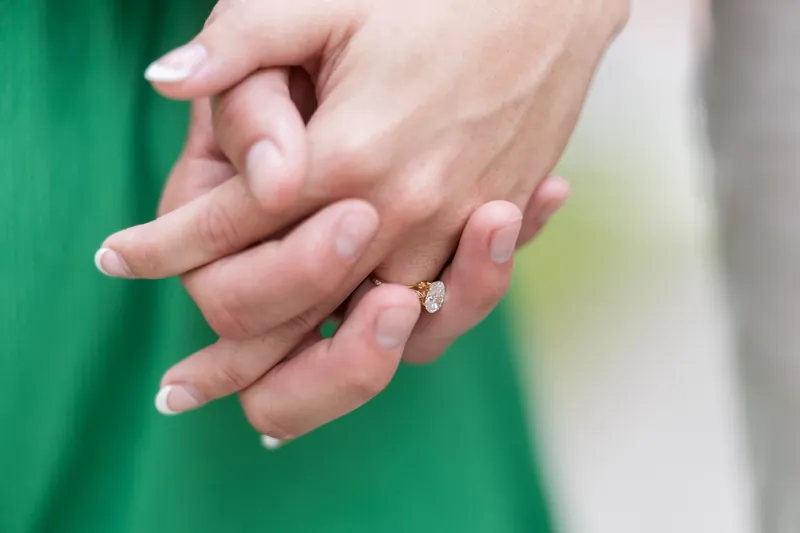Two hands with a diamond ring visible, one wearing a green sleeve and the other in neutral tones.