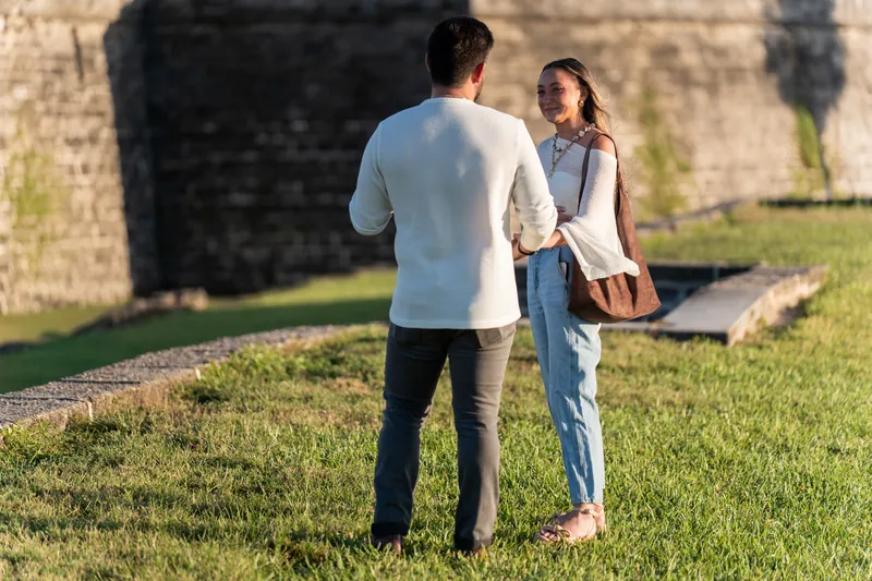 Two people face each other on the grass with the fortress wall visible behind them at Castillo de San Marcos.