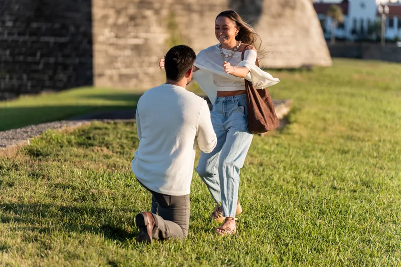 One person kneels while extending a hand toward their standing partner on the lawn at Castillo de San Marcos.