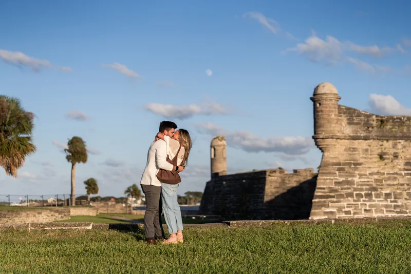 Matt and Mary kiss while standing on the lawn, the historic fort's cannons and towers framing the scene in St. Augustine.