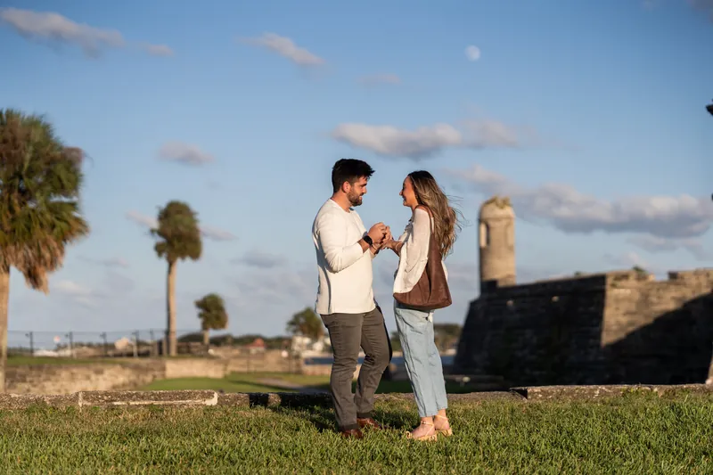 Matt holds Mary's hands as they stand facing each other on the grass with the fort's stone bastions visible across the grounds.