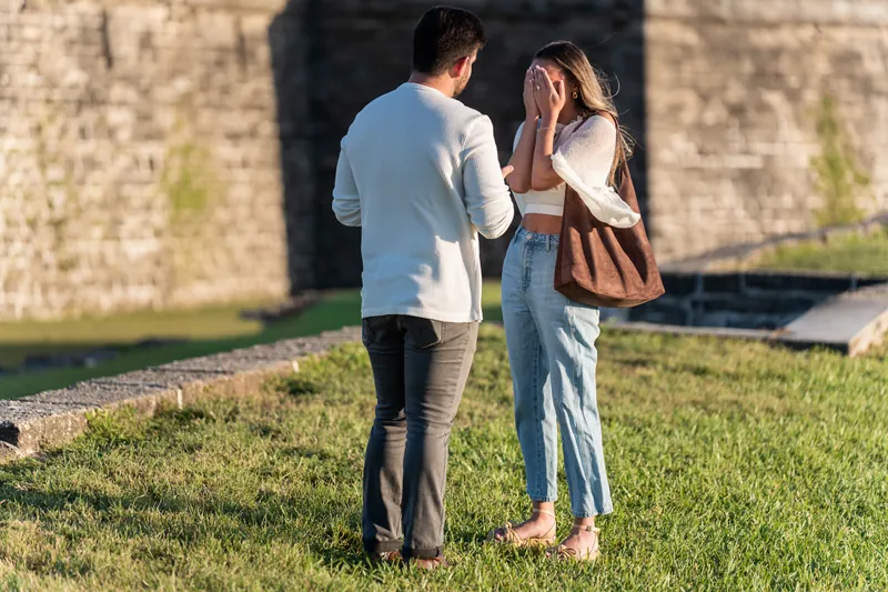 Two people stand close together on the lawn with the fort's weathered stone walls looming directly behind them in afternoon light.