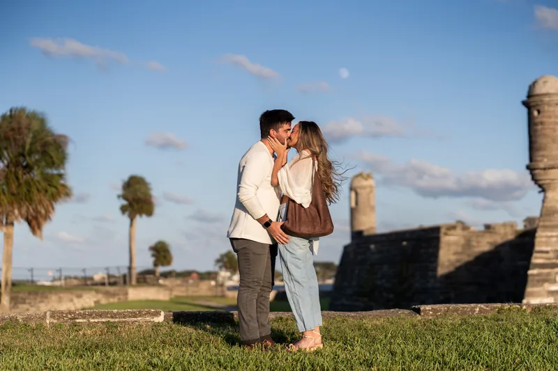 Matt and Mary kiss on the grounds of Castillo de San Marcos, palm trees and the fort's gun emplacements dotting the landscape.