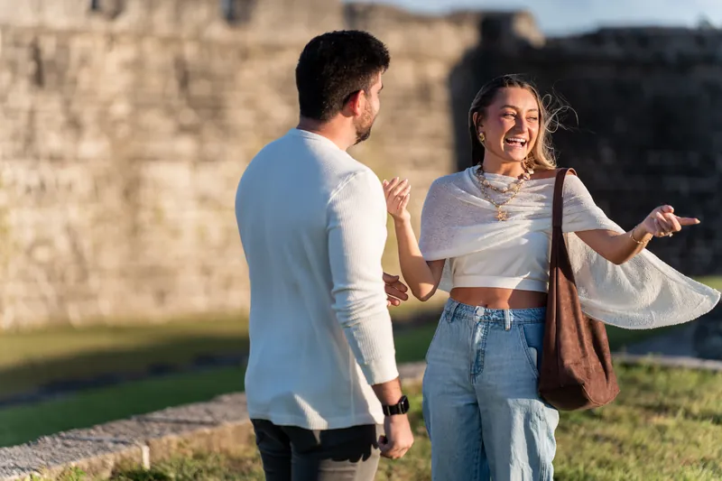A person in a white shirt smiles while facing their partner near the fort's ancient stone fortifications on a sunny afternoon.