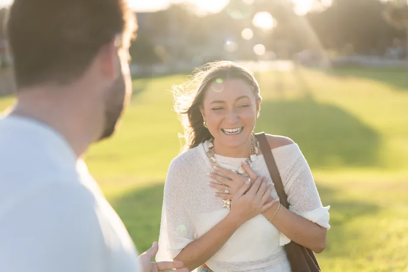 Beaming with joy, someone places a hand over their heart while facing their partner in golden afternoon light at the castle.