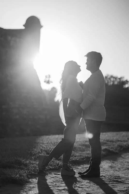 Silhouetted against sunset, a couple stands close together with the fort's bastion rising behind them.