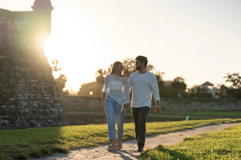 Walking toward golden light with the fortress tower framing the scene, the couple strolls across the grassy grounds.