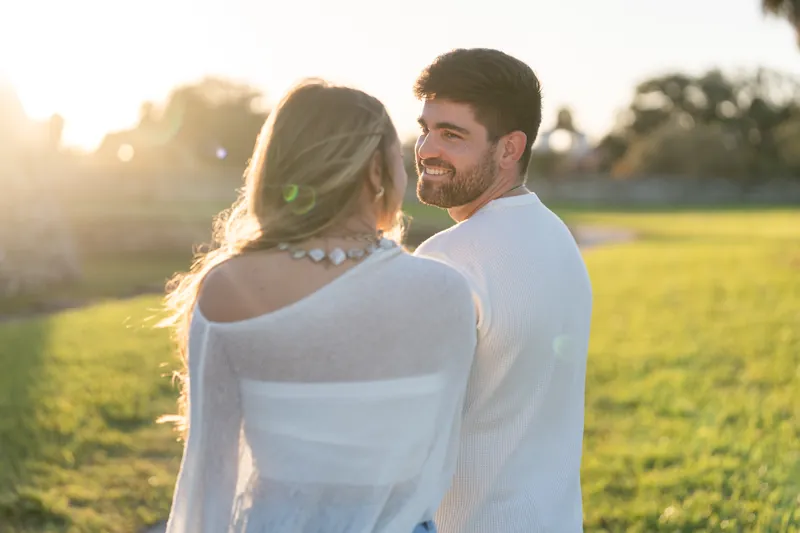 The couple embraces with the sunset glowing behind them at Castillo de San Marcos, their faces close and smiling.