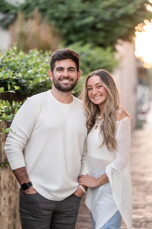 Matt and Mary stand arm in arm on a tree-lined street in downtown St. Augustine, both smiling at the camera.