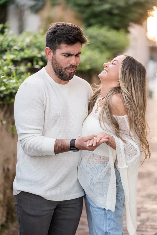 Matt and Mary stand close together on a tree-lined street in downtown St. Augustine, exchanging an intimate glance as he holds a small box.