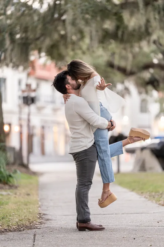Matt lifts Mary off the ground in an exuberant embrace on a quiet pathway lined with Spanish moss and colonial architecture.