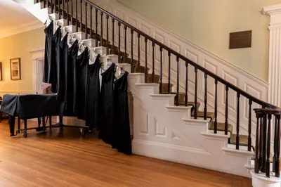 Black robes hanging on staircase railing in elegant foyer with grand piano