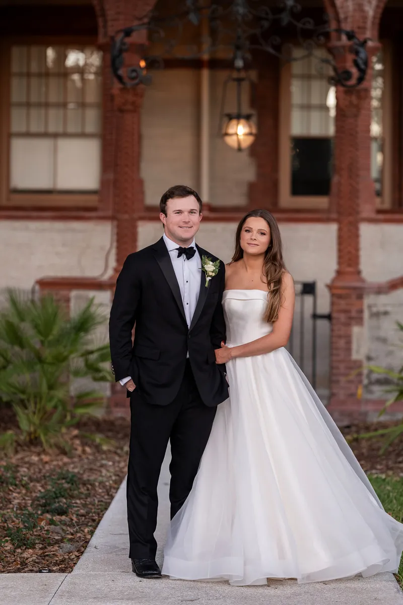 Bride in white gown holding bouquet on elegant covered porch