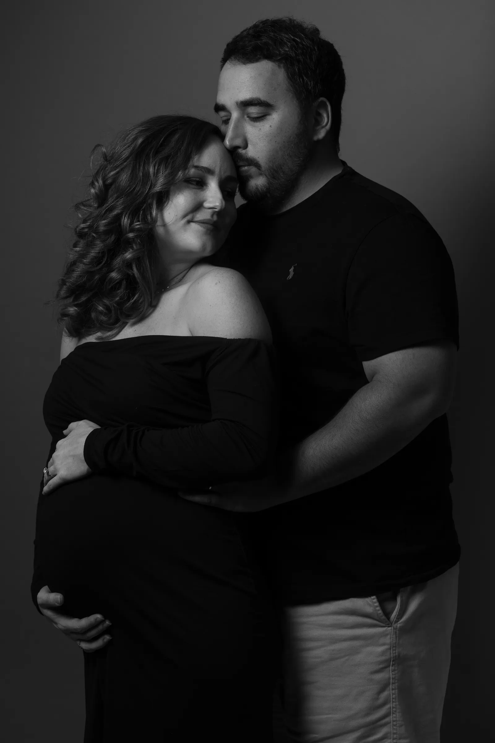 Black and white intimate couple portrait during maternity session, foreheads close together in studio.