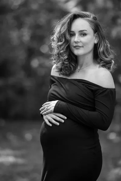 Black and white outdoor maternity portrait, expectant mother with serene expression.