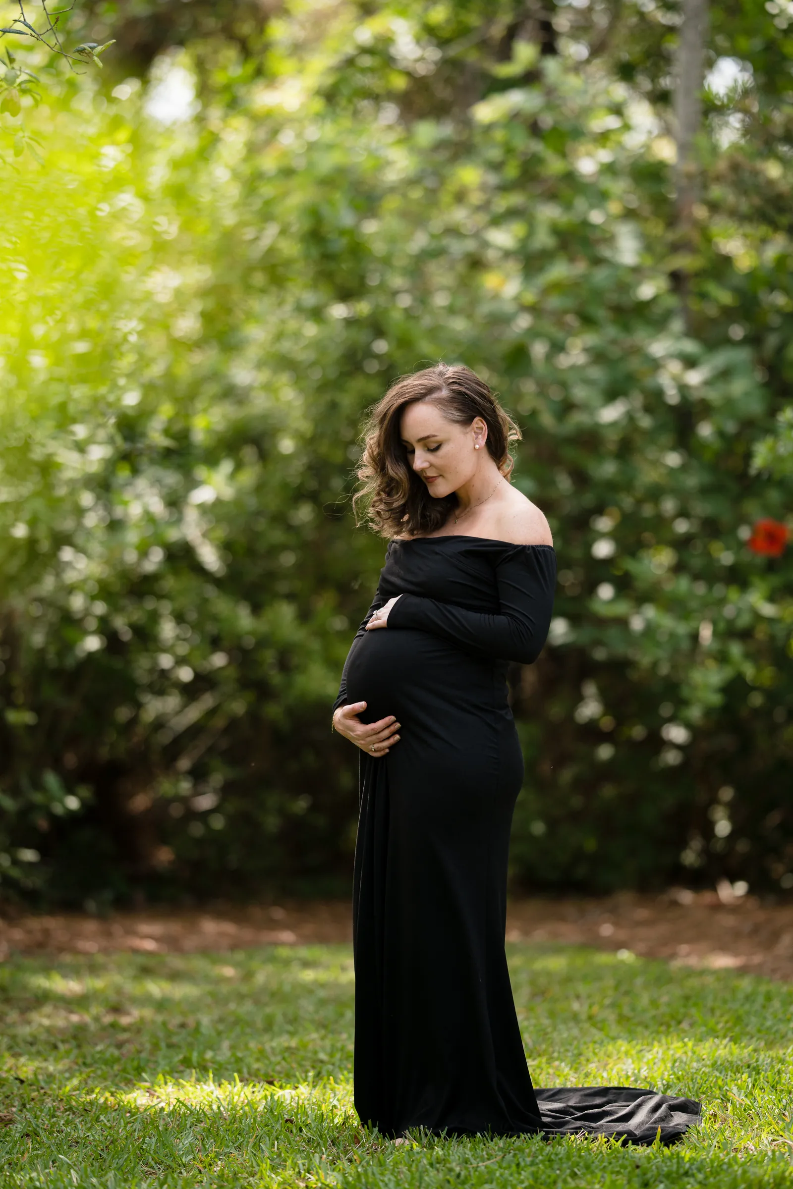 Expectant mother in garden setting, looking down at baby bump during outdoor maternity portrait.