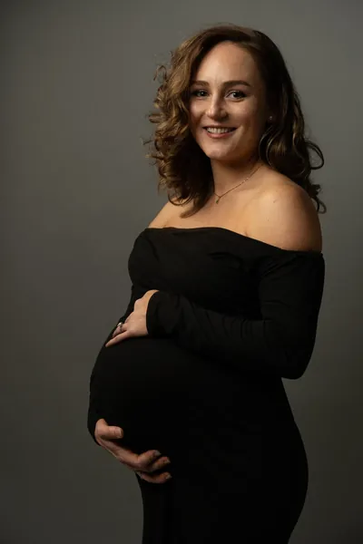 Expectant mother smiling warmly while cradling her baby bump in a black dress during studio maternity session.