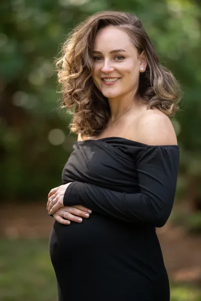Joyful outdoor maternity portrait, expectant mother smiling brightly with natural light.