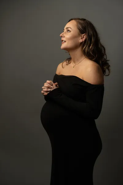 Pregnant woman in black off-shoulder dress against gray background