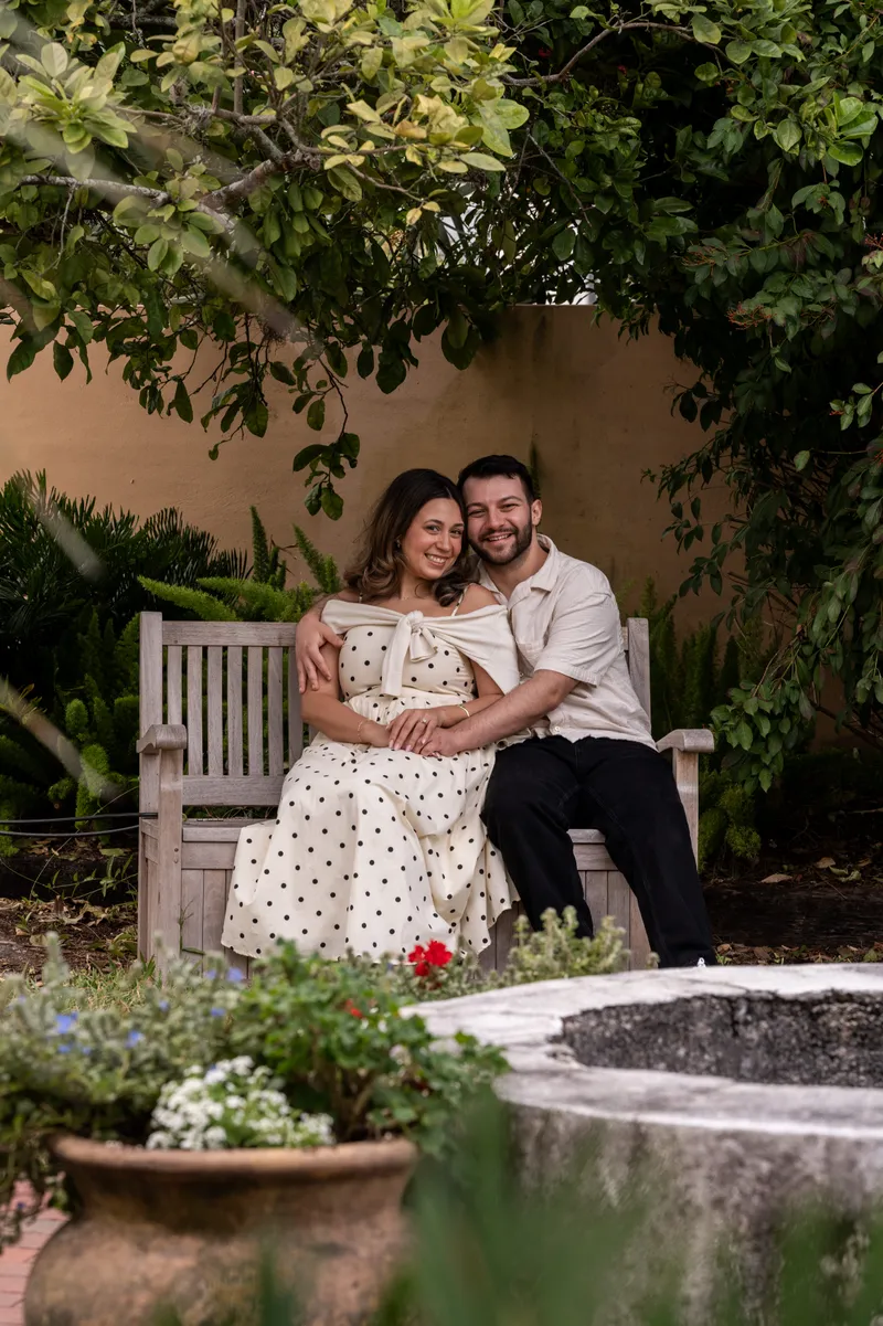 Metodija and Tiffany embrace on the stone bridge at the Lightner Museum Courtyard while someone photographs them.