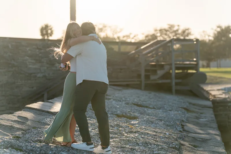 Michael and Katie embrace after the proposal on the wooden deck in warm evening light.