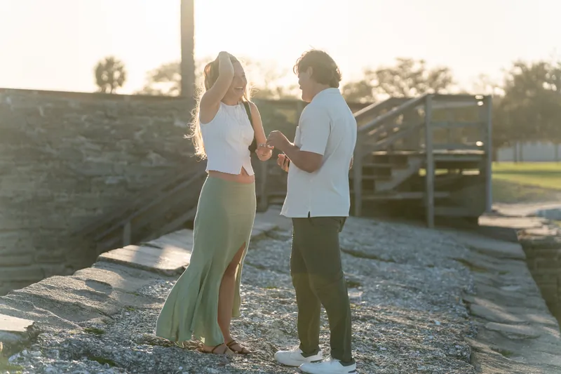 Michael and Katie stand together on the deck holding hands after the proposal at sunset.