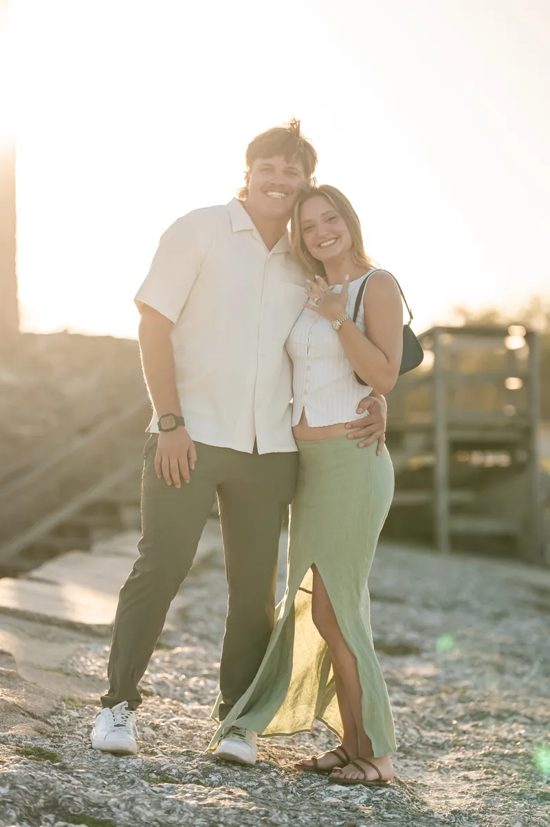 Michael and Katie stand together at sunset on a rooftop, with Michael in a cream shirt and khaki pants wrapping his arm around Katie in a light green dress.