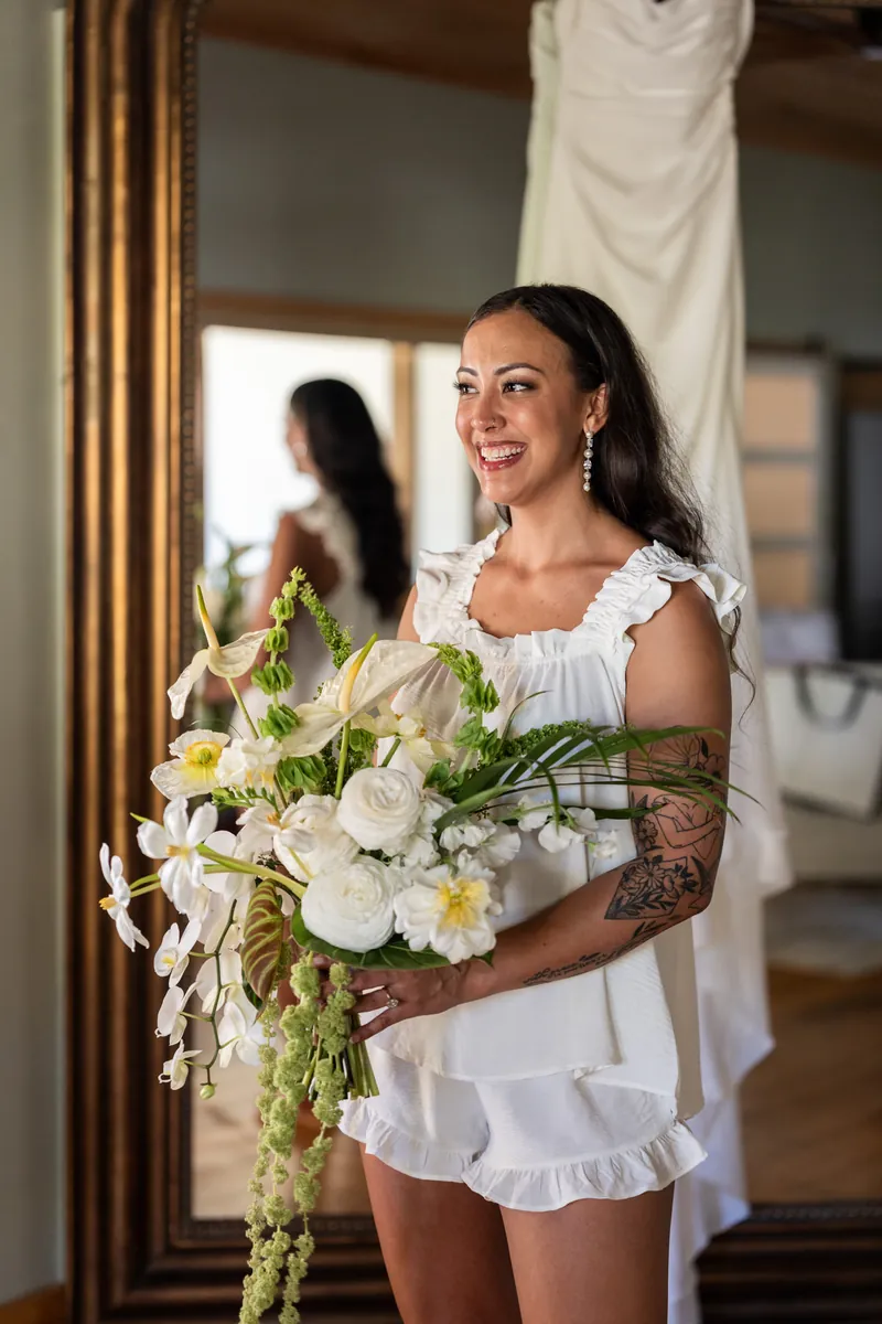 Bride holding bouquet of orchids and trailing amaranthus with dress reflected in mirror