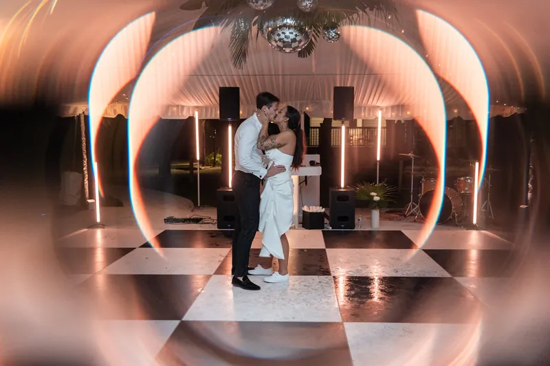Light trail portrait of couple kissing on empty checkered dance floor with disco balls